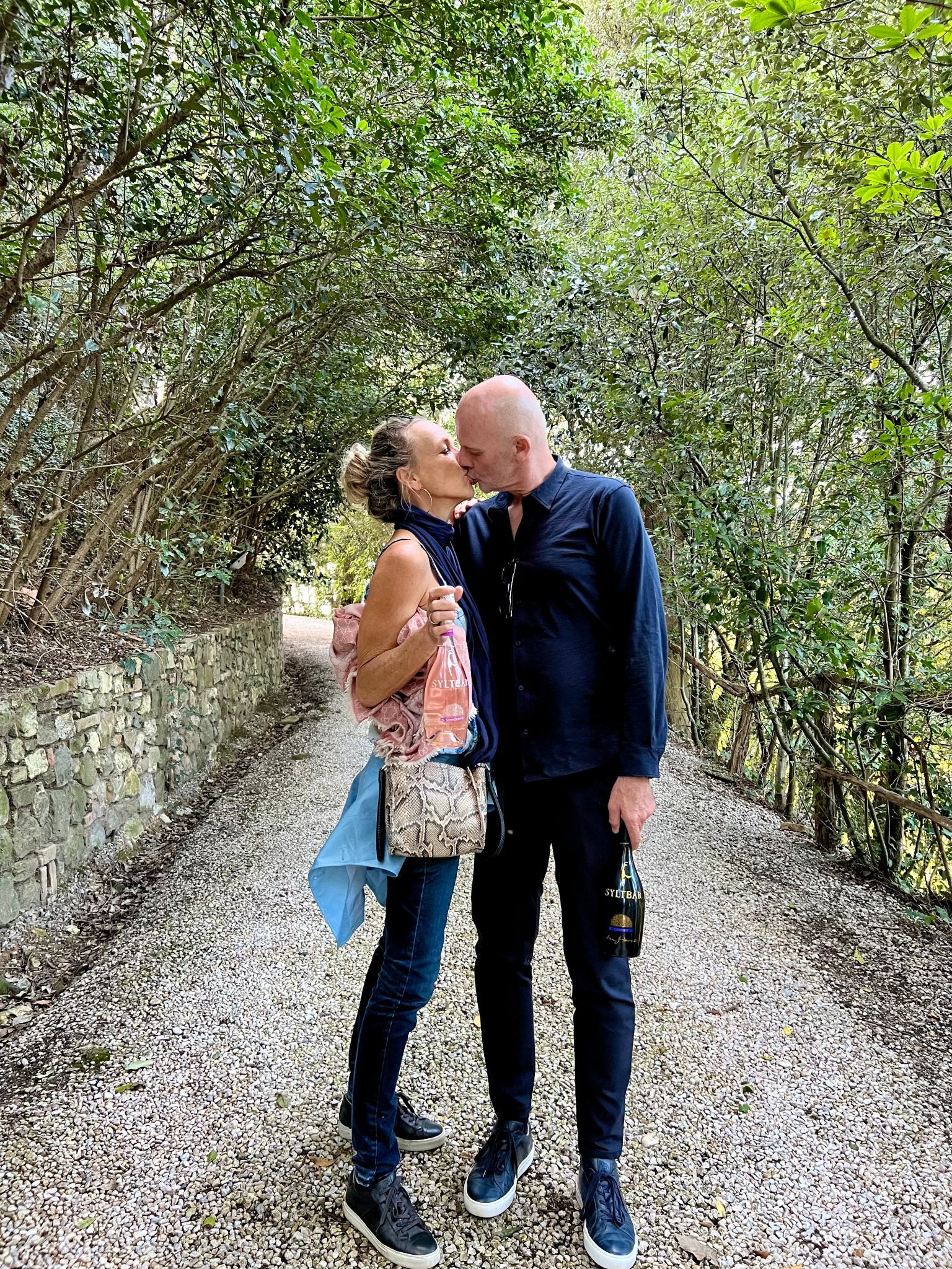 photo of SYLTBAR owners Claus and Regina kissing while each holds bottles of Mr SYLTBAR premium low-sugar prosecco and Mrs SYLTBAR low-sugar sparkling rose wine