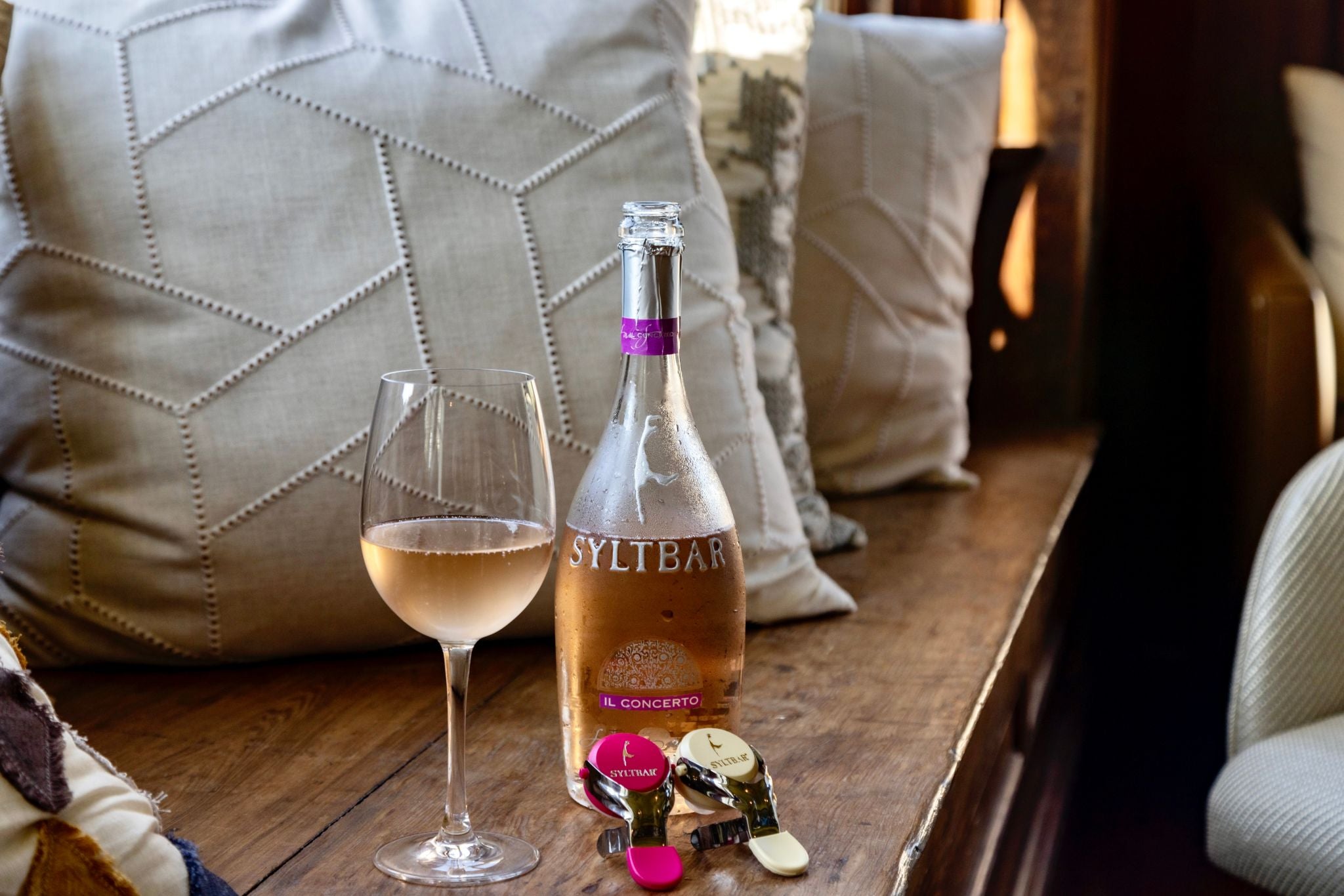 photo of a chilled bottle of SYLTBAR Mrs Sparkling rosé wine on a bench with 2 champagne bottle stoppers and a glass of sparkling wine next to the bottle